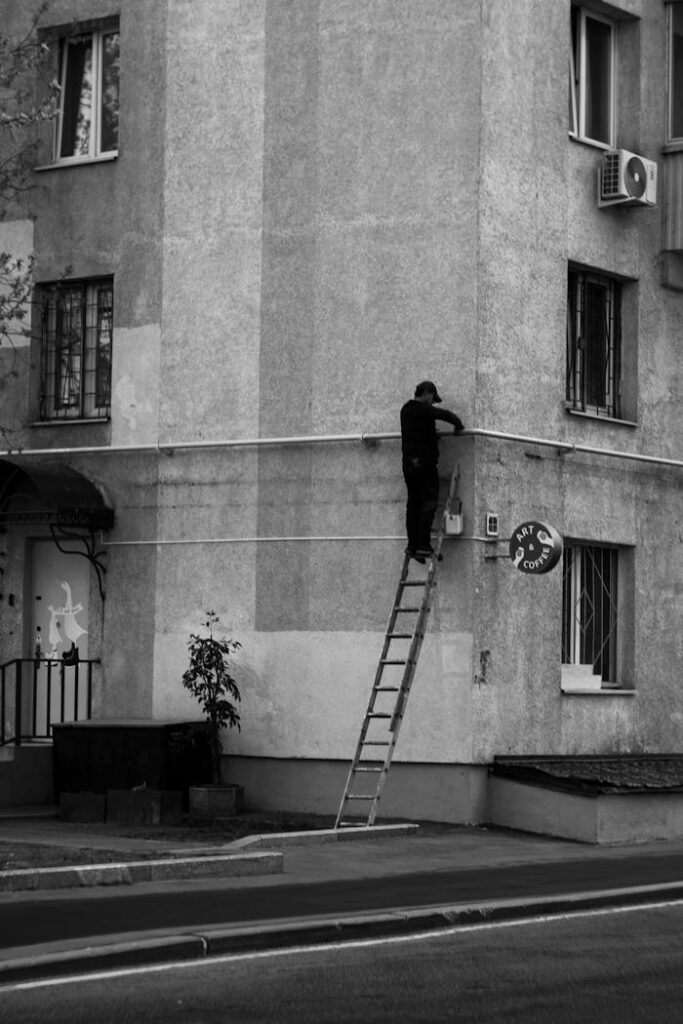Street worker on ladder fixing building facade in grayscale urban scene.